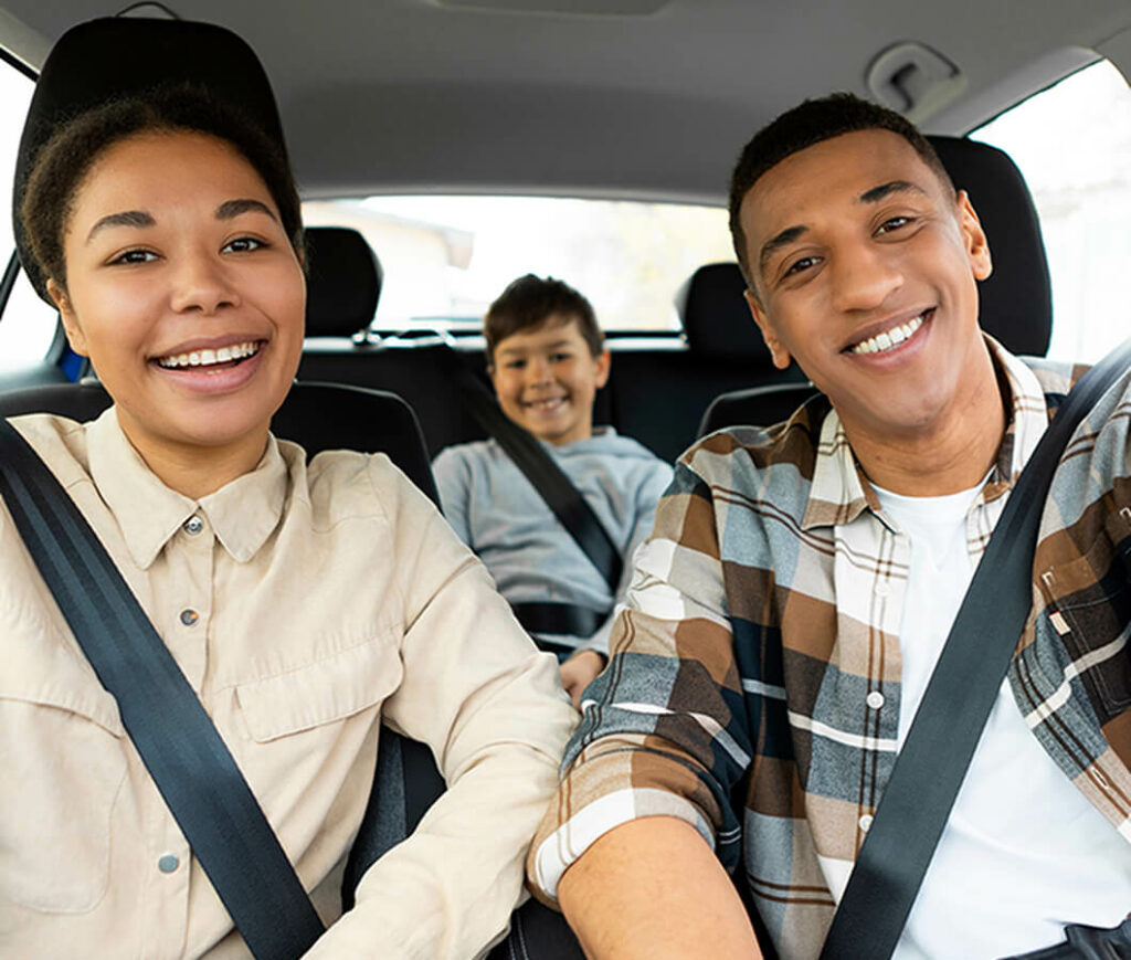 A family of three sits smiling in a car, securely buckled up, showcasing the importance of safety and savvy choices like auto insurance. The parents in casual shirts take the front seats while their son, dressed in a cozy sweatshirt, enjoys the back.