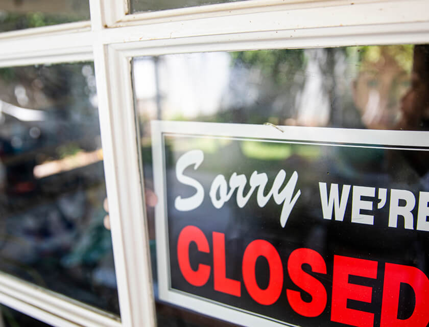 A window displays a sign reading Sorry Were Closed in bold letters. Beyond the glass, a blurred outdoor setting with greenery hints at tranquility, reminding business owners of the importance of commercial insurance to protect their investment during unforeseen shutdowns.