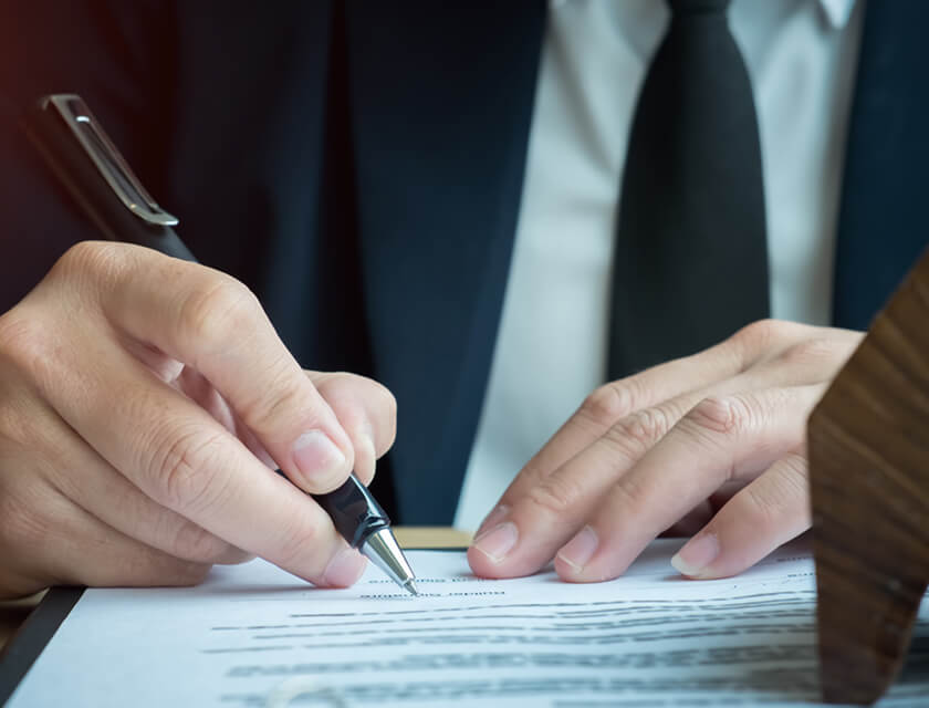 A person in a suit signs a document with precision, focusing intently on the paper. The blurred background accentuates the moment, symbolizing business or commercial insurance activity.