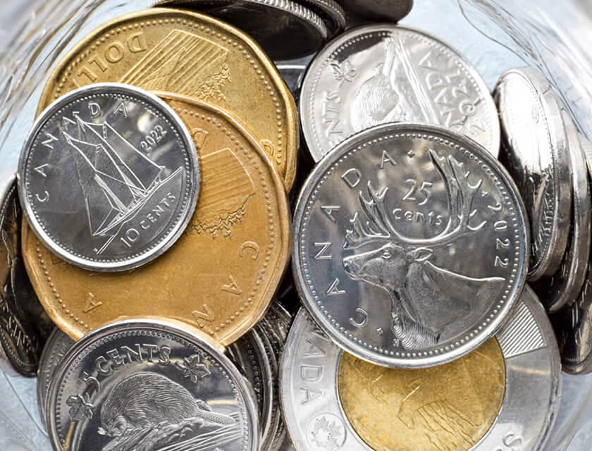 A collection of Canadian coins in a jar, featuring various denominations, much like the diverse options offered by residential insurance. Prominent coins include silver quarters with a caribou design and gold-colored one-dollar coins. Different designs and years are visible on the coins.