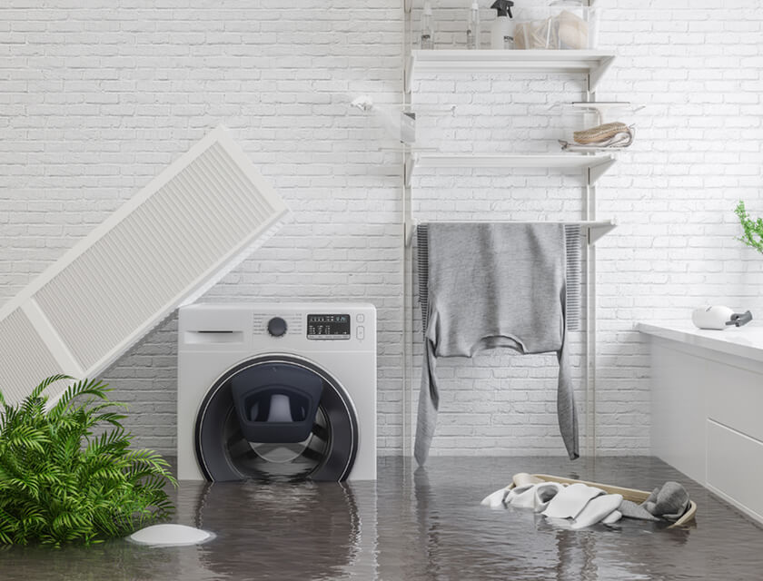 A laundry room is flooded with water, partially submerging a washing machine and a pair of sneakers. A grey sweatshirt hangs above on a shelf, surrounded by the chaos. Thankfully, residential insurance can help cover unexpected damages like these—keeping your peace of mind intact.