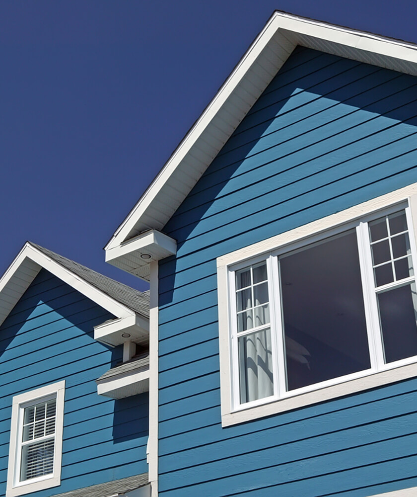 Blue house with two peaked roofs against a clear blue sky. The exterior features white-trimmed windows and horizontal siding. This modern architectural style not only showcases two sections but also emphasizes the need for robust residential insurance coverage.