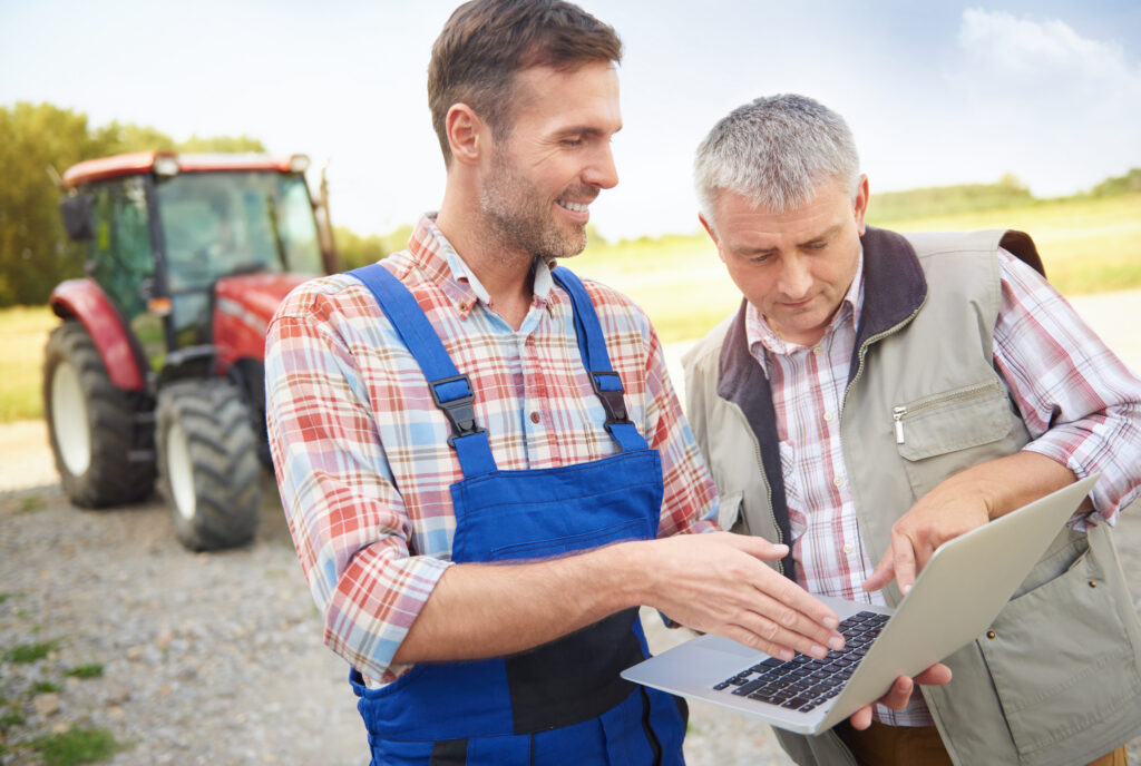 Private Insurance vs. OMAFRA: How to Build a Total Farm Safety Net 2 people discussing an agricultural plan on the laptop in the farm.