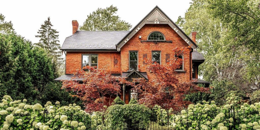 A photo of a red brick history home surrounded by greenery in Stratford, Ontario.